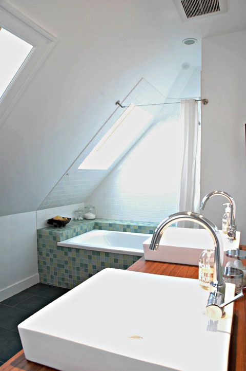 a small attic bathroom with a tub clad in blue tiles, a double wooden vanity, skylights