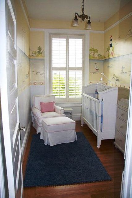 a small and cool nursery with yellow wallpaper walls, white vintage furniture and a blue rug plus a vintage chandelier