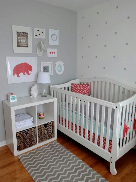 a cozy tiny nursery with a grey wall, a polka dot accent wall, a white crib, a storage unit and a small and cute gallery wall