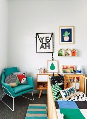 a bright mid-century modern nursery with a turquoise chair, a crib with bright bedding, a bold rug and a colorful gallery wall