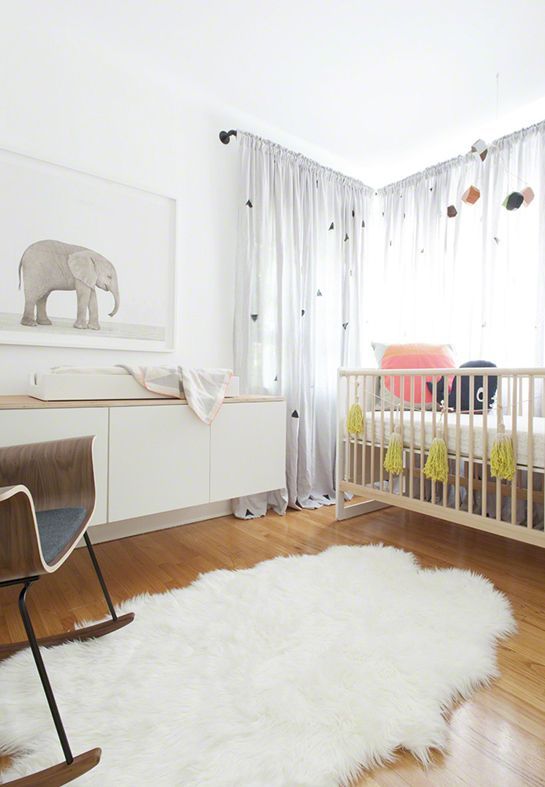 a small neutral Scandi nursery with a stained crib, a white floating dresser, a rocking chair, a rug, an artwork and some sheer curtains