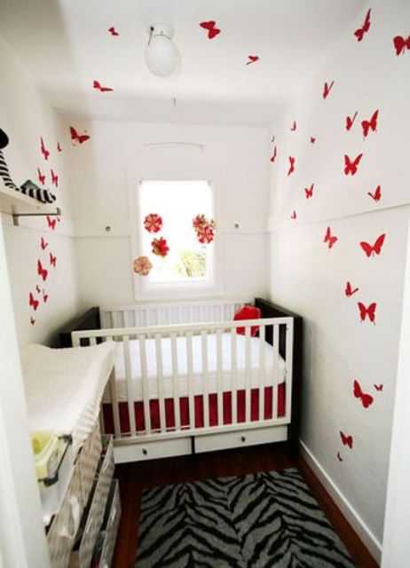 a tiny nursery with a crib and white bedding, a white dresser that is a changing table, red butterflies all over the walls is a great space to be in