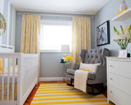 a tiny and cozy grey and yellow nursery with a grey rocker chair, a white crib, a bold rug and curtains, a white dresser for storage