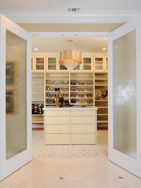 a neutral and glam walk-in closet with lots of open storage units, a warm-colored dresser, a polished pendant lamp and built-in lights