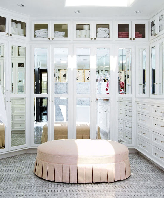 a beautiful feminine walk-in closet with mirror walls and drawers, with a pink ottoman in the center is a lovely idea