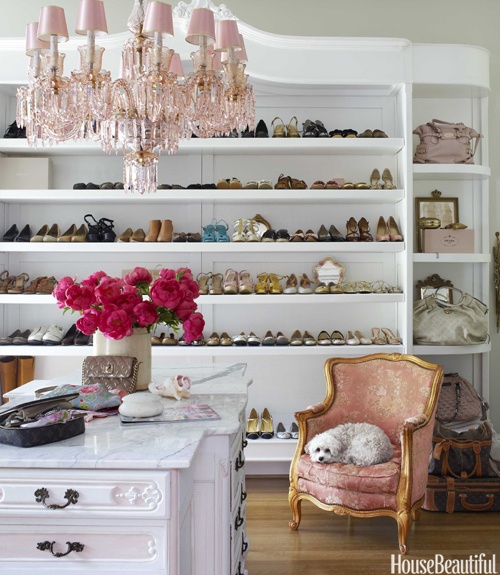a stylish feminine closet with refined vintage touches, with long shelves and bag storage, with a dresser, a pink chandelier and a pink chair