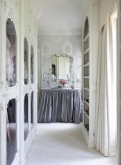 a delicate and girlish walk-in closet with white ornated frame and mirror doors plus an open storage unit and a vanity with a lilac skirt and a vintage mirror