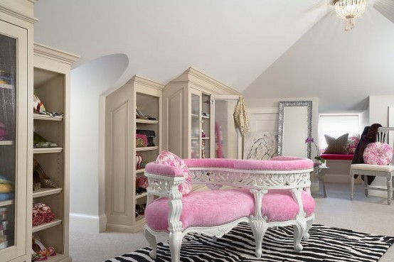 a pretty feminine walk-in closet with built-in storage units, a pink curved upholstered bench, a printed rug and some pink touches around