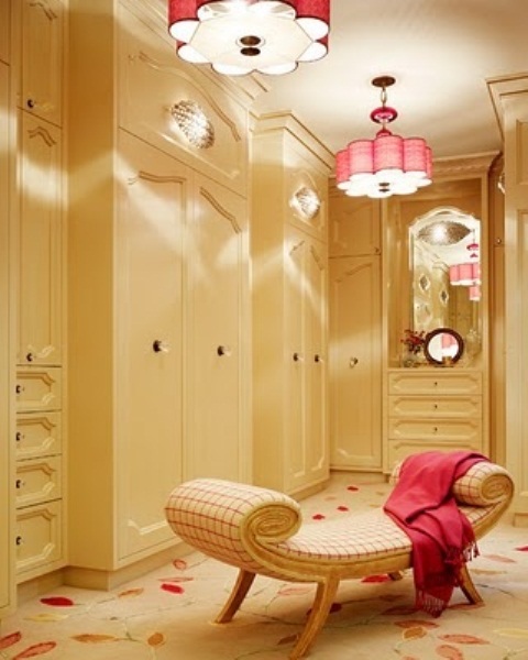 a cool warm colored feminine closet with sleek storage units and drawers, a neutral printed daybed, touches of red   pendant lamps and a blanket