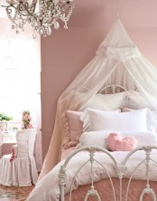 a dusty pink princess-style room with an accent wall, a metal bed with pink and white bedding and a semi sheer canopy, a crystal chandelier, a desk and a metal chair
