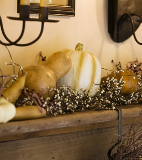 a mantel decorated with pumpkins and gourds plus blooms looks all-natural and very fall-like