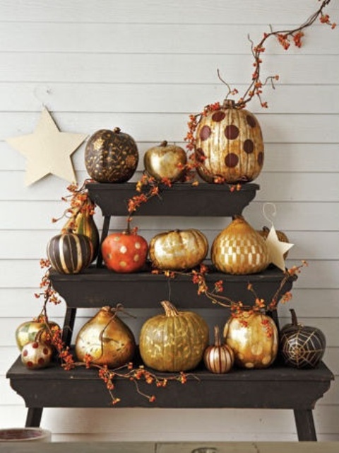 a stand with pumpkins and gourds paitned in various ways, in black and gold for fall and Halloween looks fantastic
