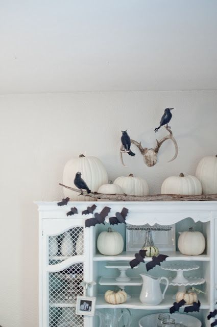 a white buffet styled for Halloween with white pumpkins, black bats and blackbirds is a great way to decorate your space for Halloween