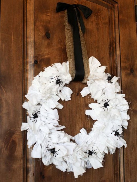 a white fabric strap Halloween wreath decorated with black spiders, with a burlap and black ribbon bow is a cool idea for Halloween