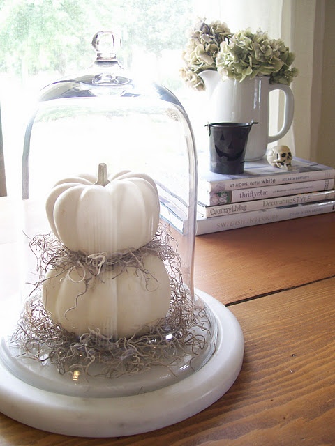 a large cloche with hay and stacked pumpkins is a cool idea to style your space for Halloween and it doesn't require any effort