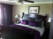 a welcoming bedroom with tan walls, dark stained furniture, grey and purple bedding and purple curtains makes a color statement
