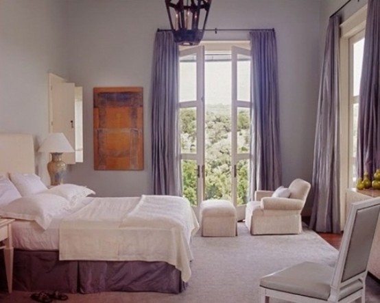 a lavender bedroom with light walls, a lavender bed skirt, a rug and purple curtains plus some white furniture is chic