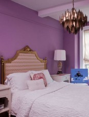 a purple bedroom with a refined bed, a unique copper chandelier, table lamps and neutral bedding looks whimsical
