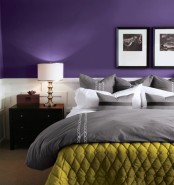 a bold purple bedroom with white paneling, grey and white bedding, a mustard blanket, dark stained furniture and chic artworks