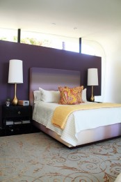 a deep purple accent wall, black nightstands, table lamps with gold bases, an ombre bed and bright bedding