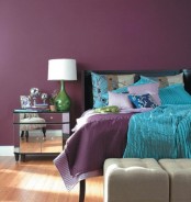 a purple bedroom with a black bed, neutral ottomans, mirror nightstands, table lamps with green bases and shiny accessories here and there