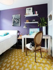 a colorful bedroom with a deep purple accent wall, white furniture, an artwork and a bold carpet on the floor just wows