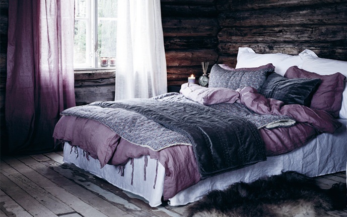 a rough wooden bedroom with white and purple bedding and curtains is a fresh take on a classic chalet bedroom