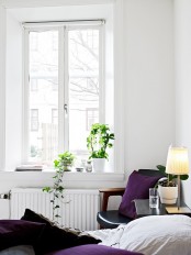 a neutral Scandinavian bedroom with a black leather chair, purple bedding and some potted plants and a table lamp
