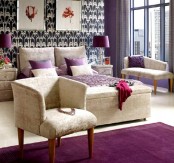 a purple and tan bedroom with printed wallpaper, tan upholstered furniture, artworks and table lamps plus purple textiles