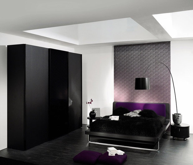 a bold bedroom with black furniture and a lamp, skylights and some purple textiles to add color to this space