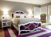 a bright bedroom with a carved bed with purple decor, a striped rug, green furniture pieces and accessories plus mirror nightstands