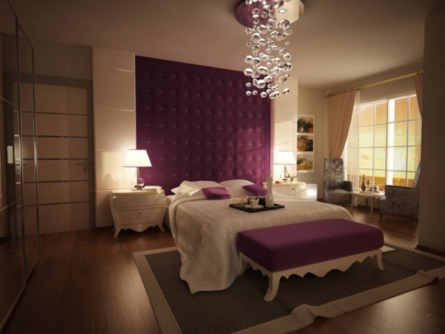 a neutral bedroom with a purple upholstered wall, purple pillows and a bench plus a bubble chandelier accenting the ceiling