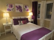 a tan bedroom with white furniture, purple floral artworks and pillows, purple curtains and bedding is a stylish and cool space