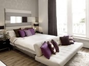 a monochromatic bedroom in grey and white, with cozy upholstered furniture, purple and white pillows, purple curtains for a touch of color
