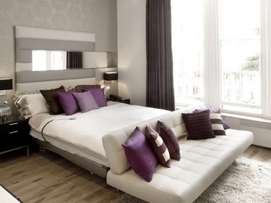 a monochromatic bedroom in grey and white, with cozy upholstered furniture, purple and white pillows, purple curtains for a touch of color