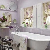 a girlish bathroom with lavender walls, a white vintage bathtub, florla curtains, exquisite mirrors and a forged table