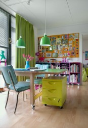 a super bright home office done with a green desk, blue chair, yellow file cabinet, a fuchsia bookshelf and an orange memo board, green curtains and green pendant lamps