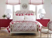 a country chic red and white bedroom with red dressers, a neutral bed with printed upholstery and red and white bedding, a neutral chair with red touches