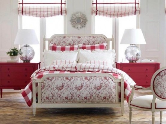 a country chic red and white bedroom with red dressers, a neutral bed with printed upholstery and red and white bedding, a neutral chair with red touches