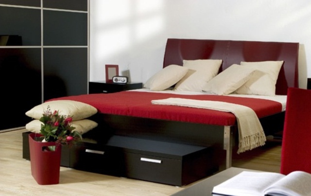 a black shiny storage unit, a burgundy bed with red and creamy bedding, a black storage bench and black nightstands