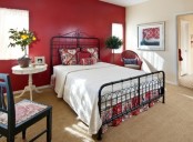 a bedroom with a deep red accent wall, a black forged bed, a white side table and a black chair with red and white upholstery, potted plants