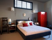 a grey bedroom with a black bed, neutral bedding, matching nightstands, a ladder, a red set of lockers and some stools