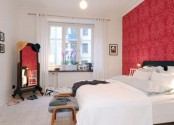 a catchy bedroom in white accented with a red wallpaper wall, a black bed and white bedding, a mirror and some accessories as part of decor