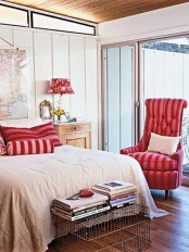 a neutral bedroo with shiplap walls, a bed with red and white bedding, a red chair and some red table lamps and a small bench