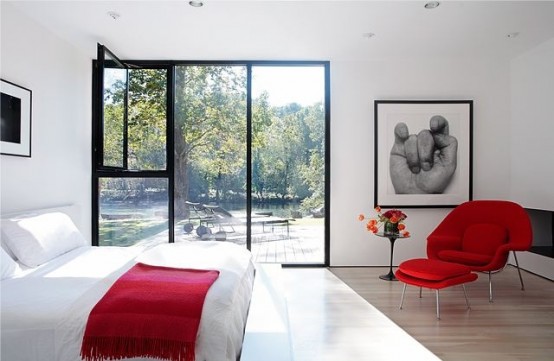 a neutral bedroom accented with black frames and red touches, a red chair and a red blanket looks cool and chic and catches an eye