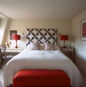 a neutral bedroom with white nightstands, a white bed, red table lamps, a red upholstered bench and bold artwork