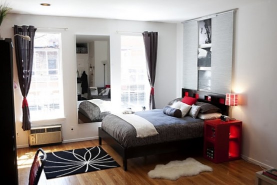 a monochromatic bedroom with grey and white bedding and textiles, with a red nightstand and red pillows