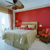 a neutral bedroom with a red accent wall, a wicker chair with red and gold stripes and red and gold striped pillows