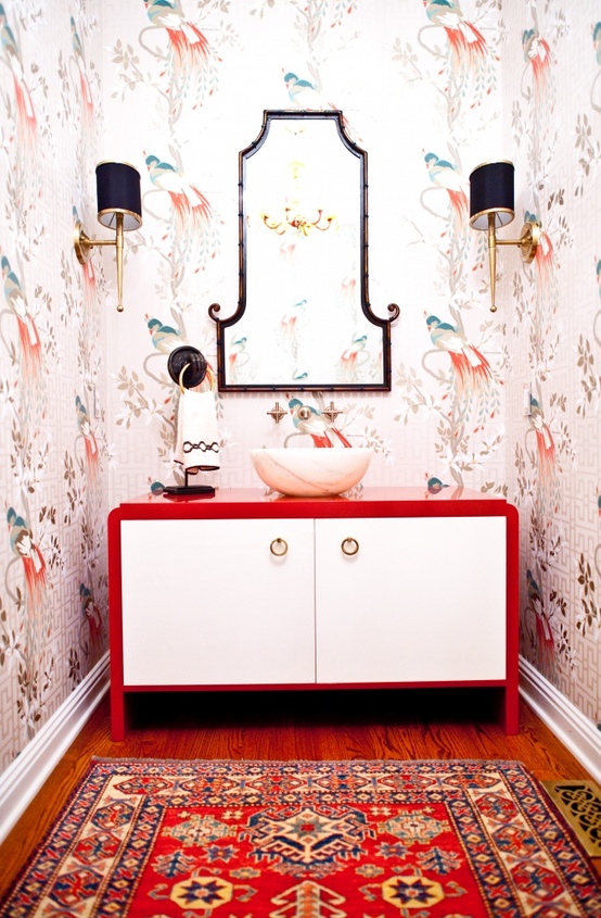 trendy flora and fauna wallpaper, a red vanity, a red rug and a chic mirror and wall sconces