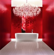 a refined bathroom with red walls, a large crystal chandelier, an oval tub and nothing else looks dreamy